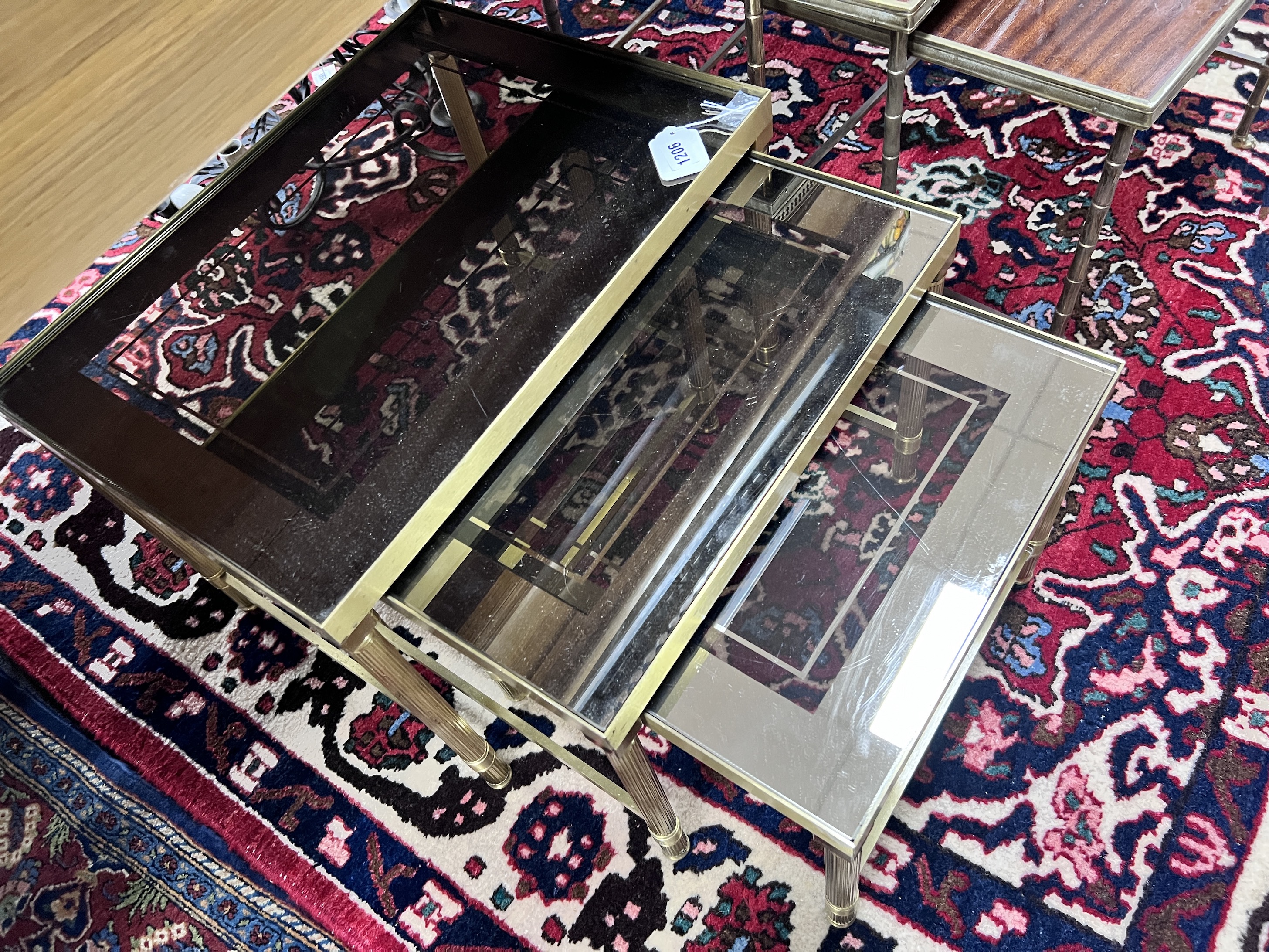 A nest of three 'Maison Charles' style brass and smoked glass topped tables, largest width 50cm